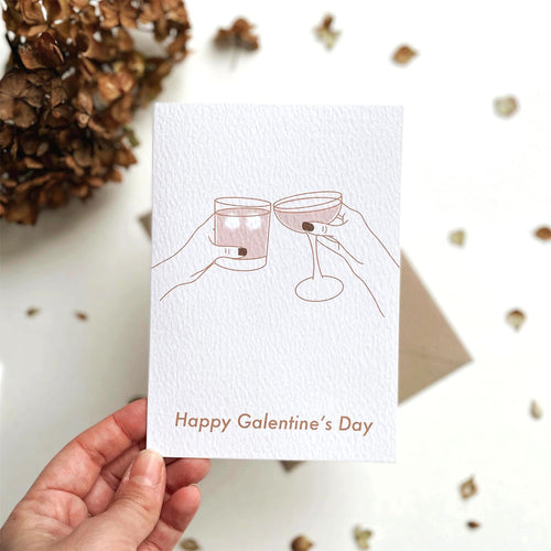 Happy Galentine's Day card by Megan Heloise. Featuring and illustration of feminine hands clinking glasses.